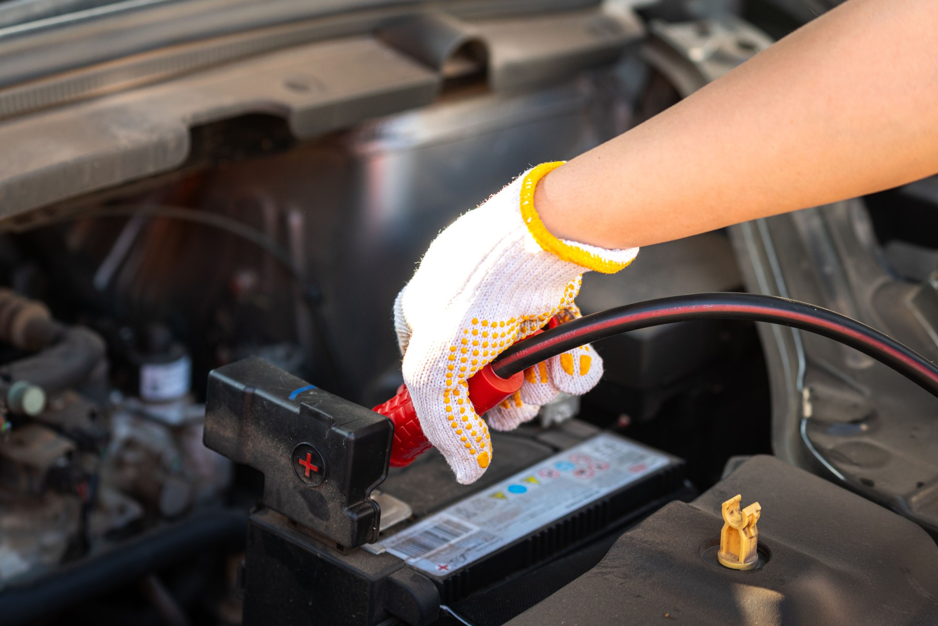 Action of a technician hand is using an emergency clamping kit to clamp on positive polar for jumping the 12V car battery.